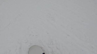 Bir snowboardcu karlı bir yamaçtan aşağı iniyor, ağaçlar kenarlarını kaplıyor..