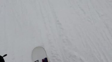 Bir snowboardcu karlı bir yamaçtan aşağı iniyor, ağaçlar kenarlarını kaplıyor..
