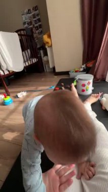 Arka planda oyuncakları olan pijamalı bir bebek anne pov ile oynuyor.