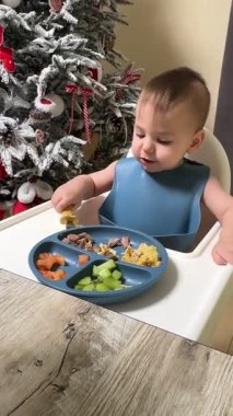 Arka planda Noel ağacı olan Yüksek Sandalyede Bebek Yeme