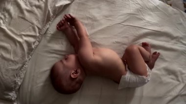 Bebek bezi takmış, yatak manzarasında geriniyor.