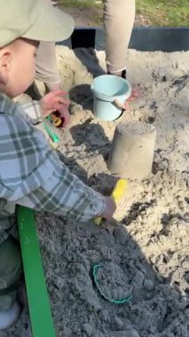 Çocuk babasıyla kum havuzunda oynuyor.