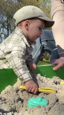 Çocuk babasıyla kum havuzunda oynuyor.