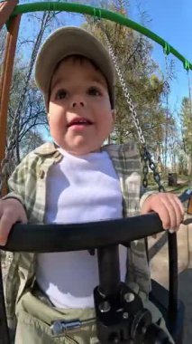 Yürüyen çocuk güneşli bir parkta salıncağın tadını çıkarıyor.