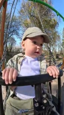 Yürüyen çocuk güneşli bir parkta salıncağın tadını çıkarıyor.