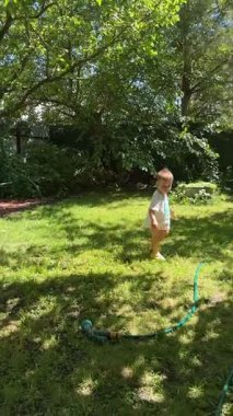 Küçük çocuk yaz mevsiminde bahçe hortumuyla eğleniyor.