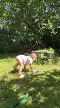 Küçük çocuk yaz mevsiminde bahçe hortumuyla eğleniyor.