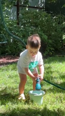 Küçük çocuk yaz mevsiminde bahçe hortumuyla eğleniyor.