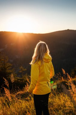 Sarı ceketli kadın yürüyüş sırasında gün batımını seyrediyor. Doğadaki macera