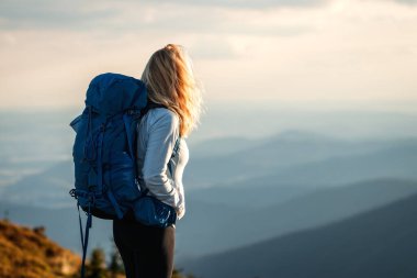 Sırt çantalı bir kadın dağlarda yürüyüş yapıyor. Doğada yürüyüş yapan bir gezgin. Dağ sırasının güzel manzarası