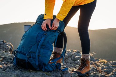 Dağ zirvesine çıktıktan sonra sırt çantasını açan kadın. Dışarıda yürüyüş yapmak. Bayan turist sırt çantalarını boşaltıyor.