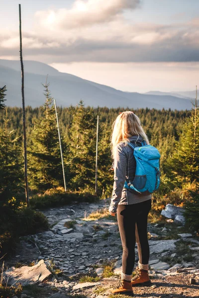 Dağlarda yürüyüş yapan bir kadın var. Sırt çantalı kadın turist dağların üzerinden gökyüzüne bakıyor.
