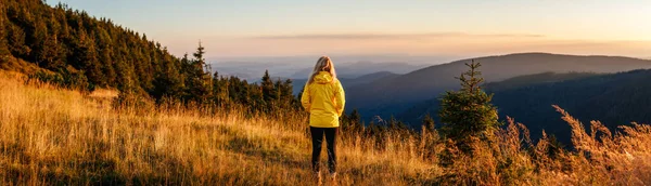 Woman looking at mountain range in natural parkland Jeseniky during sunset. Panoramic landscape with hiking tourist