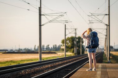 Sırt çantalı kadın gezgin tren istasyonunda trenini bekliyor. Yaz tatilinde yalnız seyahat eden kadın turist.