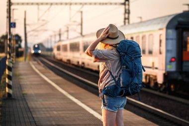 Trenle seyahat et. Sırt çantalı bir kadın tren istasyonunda duruyor ve gelen trene bakıyor.