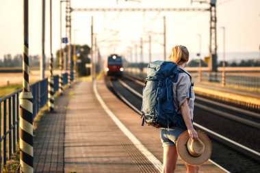Sırt çantalı gezgin tren istasyonunda duruyor ve gelen trene bakıyor.