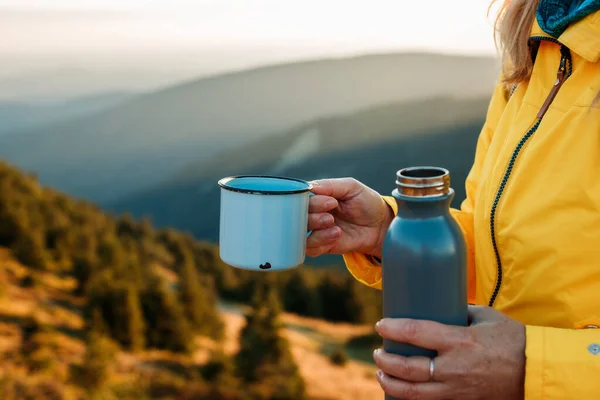 stock image Refreshment after successfully climbed mountain summit. Female hiker drinking hot drink from travel mug and enjoying view at mountains during sunset