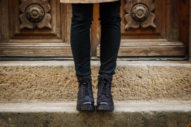 Modaya uygun siyah çizme. Yakın plan şık deri ayakkabı. Caddede merdivenlerde duran kadın bacakları.