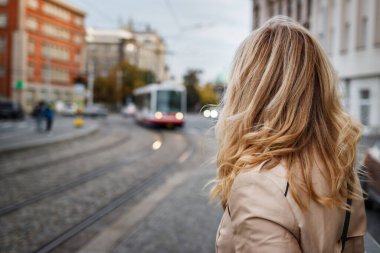 Otobüs durağında tramvay bekleyen bir kadın. Şehir sokağına gelen tramvaya bakan bir yolcu. Toplu taşıma