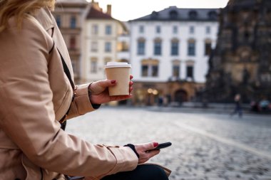 Şehir molası sırasında akıllı telefon kullanan bir kadın. İş kadını kahve içiyor ve cep telefonuna mesaj atıyor.