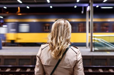 Tren istasyonundan geçen bir kadına bakıyor. Toplu taşıma. Trenle seyahat et. Gece şehir hayatı