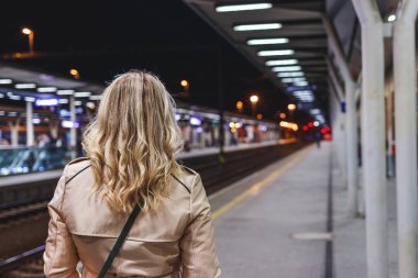 Tren istasyonunda tren bekleyen bir kadın. Toplu taşıma. Trenle seyahat eden bir yolcu. Gece şehir hayatı