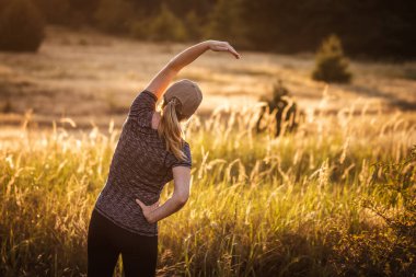 Kadın gün batımında dışarıda egzersiz yapıyor. Doğada koşmadan önce ısınma egzersizi yapıyorum. Fitness aktif yaşam biçimi