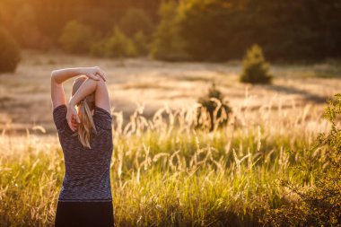 Açık havada koşmadan önce ısınma egzersizi yapıyorum. Kadın gün batımında koşuya hazırlanıyor. Spor ve aktif sağlıklı yaşam tarzı