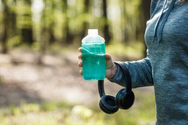 Şişeden su içen ve kulaklık tutan bir kadın. Ormanda koşarken ve koşarken dinleniyor. Spor ve spor aktiviteleri