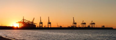 Gdansk Limanı 'nda gün batımında ticari rıhtım ve vinçlerle. Baltık Denizi 'ndeki Stogi plajından panoramik manzara. Sanayi limanının silueti