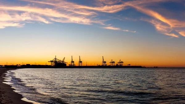 Gdansk limanında günbatımında ticari rıhtım ve vinçlerle. Baltık Denizi 'ndeki Stogi plajından görüntü. Sanayi limanının silueti