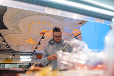 Sebze arayan bir adam ön planda alışveriş yapan erkek müşteriler bir mağazada raflardır.