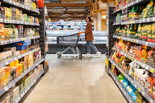 Eine Frau Mit Einem Einkaufswagen Geht Zwischen Regalreihen Einem Lebensmittelgeschäft — Stockfoto