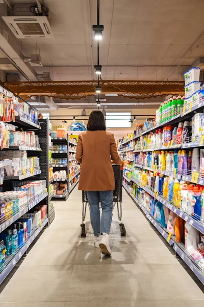 一个带着购物车后视镜的女人走在杂货店的一排货架之间 — 图库照片