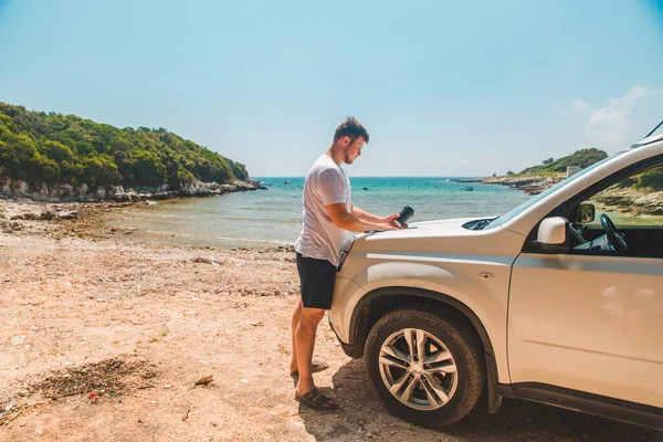 男子在地图上查看汽车引擎盖目的地位置背景夏季海滩 — 图库照片