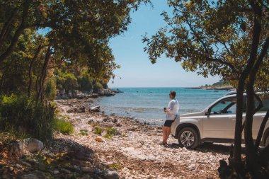 Yaz Denizi Sahili Özgürlük Seyahat Konsepti 'nde beyaz SUV arabasının yanındaki adam.