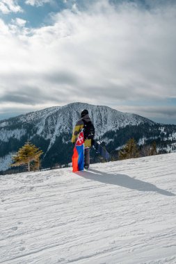 Slovakya bayrağı taşıyan snowboardcu kayak merkezinin yamacında arka planda güzel dağlar var.