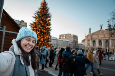 beautiful smiling women taking selfie picture at city square christmas tree on background copy space