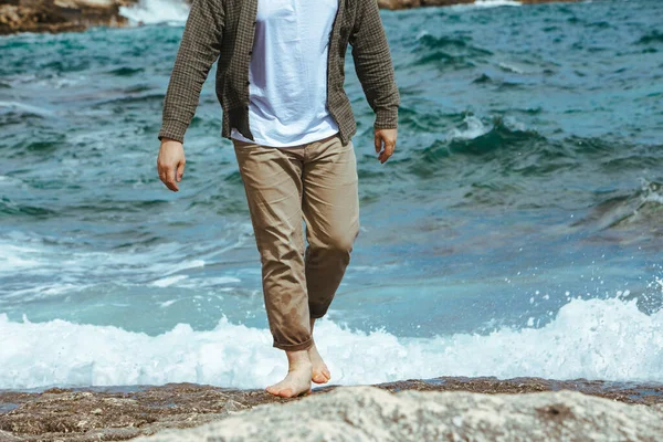wet man legs in pants walking by sea rocky beach enjoying water. summer vacation