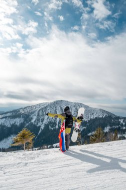 Slovakya bayrağı taşıyan snowboardcu kayak merkezinin yamacında arka planda güzel dağlar var.