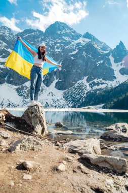 A woman with Ukrainian flag is standing on the shore of a lake. Morskie Oko, Tatras mountains, Poland