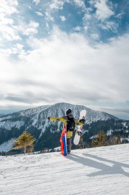 Slovakya bayrağı taşıyan snowboardcu kayak merkezinin yamacında arka planda güzel dağlar var.
