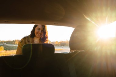 Kadın arabasının bagajından bir şeyler çıkarırken gülümsüyor.