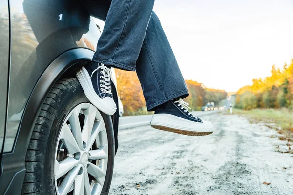 stock image womens legs hang from hood of car, autumn road is visible in background