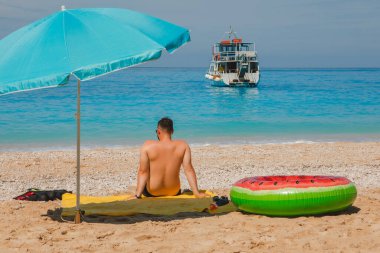 Deniz kıyısında güneşli bir günde güneşli bir şemsiye Yunan tatil gezisi arka planda küçük bir tekne.