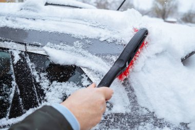 Adam yoğun kar yağışı sonrası arabasını karla kaplıyor.