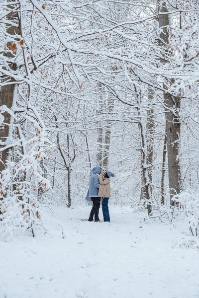 in snowy forest man circles woman in his arms as he embraces her