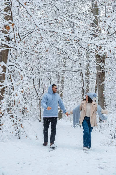 In forest full of winter snow, couple in love runs