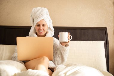 Sabah duştan sonra bir fincan kahveyle internette sörf yapan gülümseyen bir kadın.