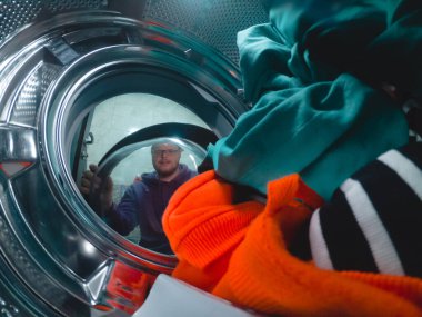 a man looks through the washing machine door at dirty clothes